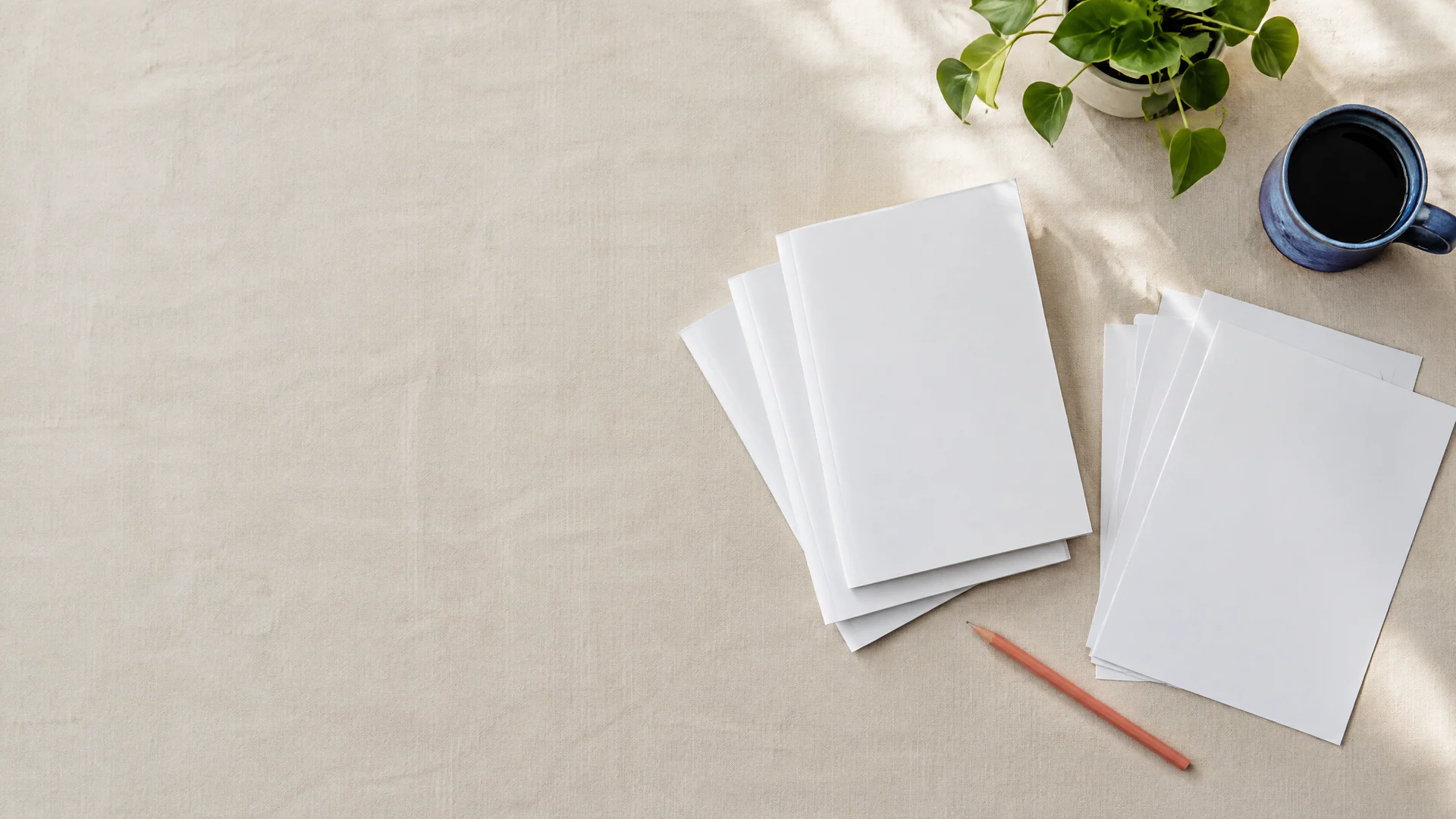 Blank printed booklets and sheets on a cream linen desk with a pencil and mug